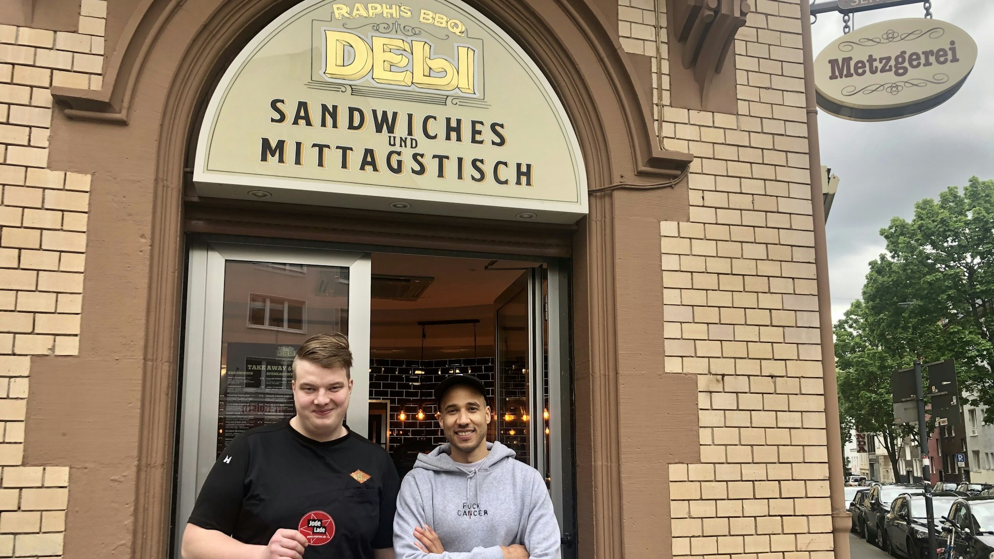 Moritz Issinger und Saloum Doucouré stehen vor dem Eingang ihres Delis in der Kölner Südstadt.