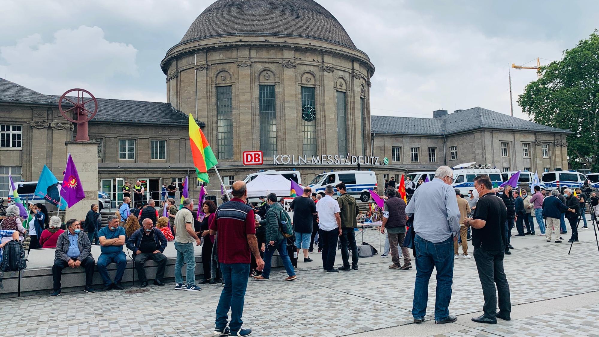 Demo-Teilnehmer stehen in Köln-Deutz mit Flaggen vor dem Bahnhof.