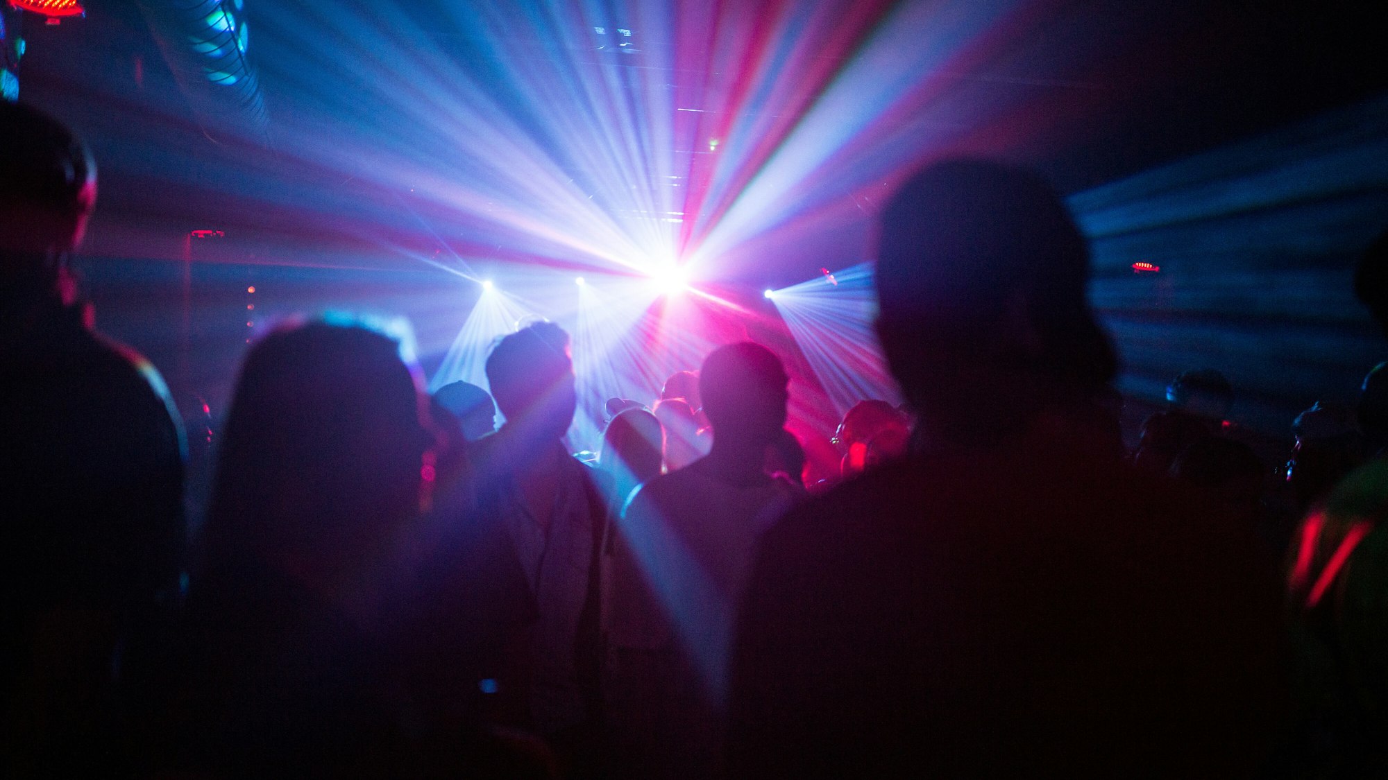 Menschen feiern in dem Symbolbild in einer Disco, Silhouetten sind im Laser-Licht zu sehen. Eine Reiserückkehrerin aus Mallorca sorgte in einem Club in Karlsruhe für einen Corona-Ausbruch.
