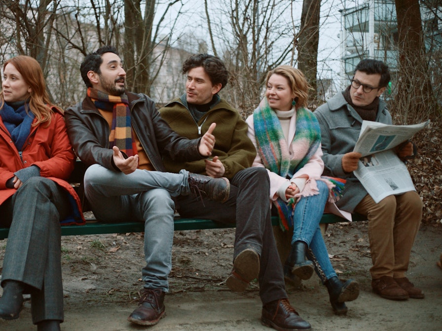 Eko Fresh und weitere Schauspieler der neuen Serie „Das Streben nach Glück“ sitzen bei Dreharbeiten zusammen auf einer Bank.