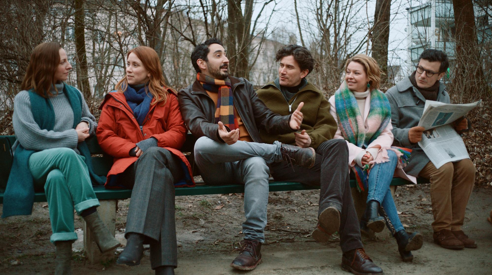 Eko Fresh und weitere Schauspieler der neuen Serie „Das Streben nach Glück“ sitzen bei Dreharbeiten zusammen auf einer Bank.