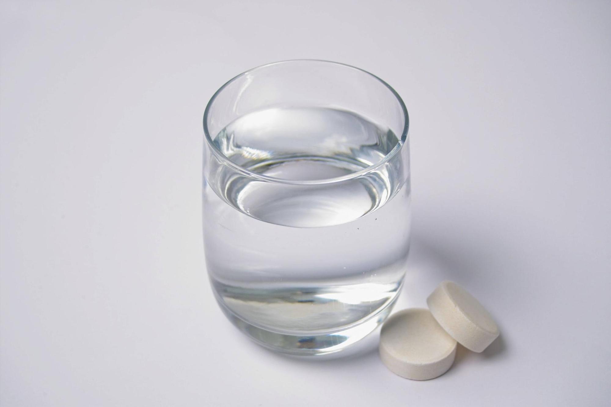 Das Symbolbild zeigt ein Wasserglas mit zwei Tabletten, die daneben liegen. Der Hersteller Abtei ruft bestimmte Vitamin-Präparate zurück, die bundesweit verkauft wurden.