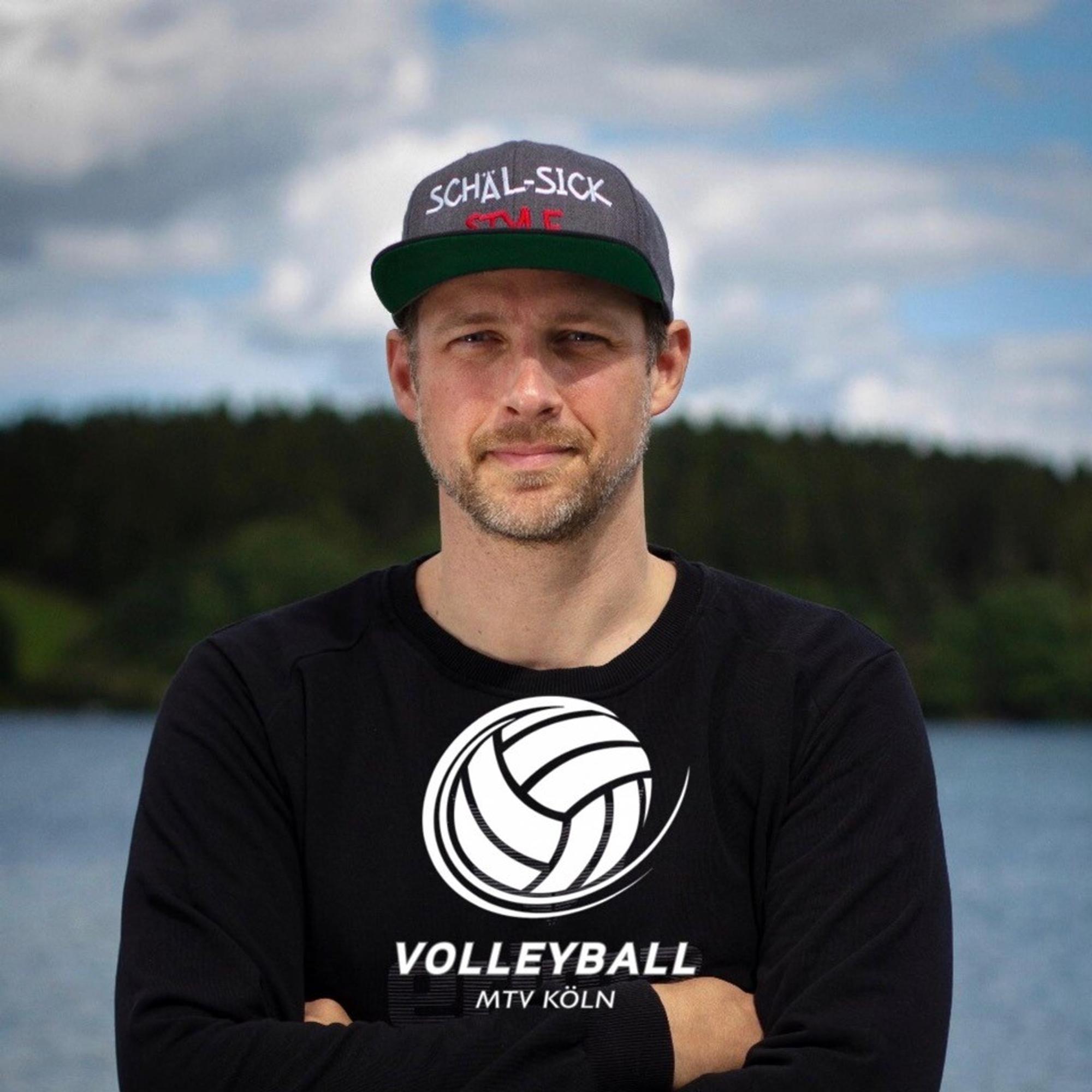 Der Kölner Kai Vogel steht mit einem Volleyball-Pullover vor dem Rhein.