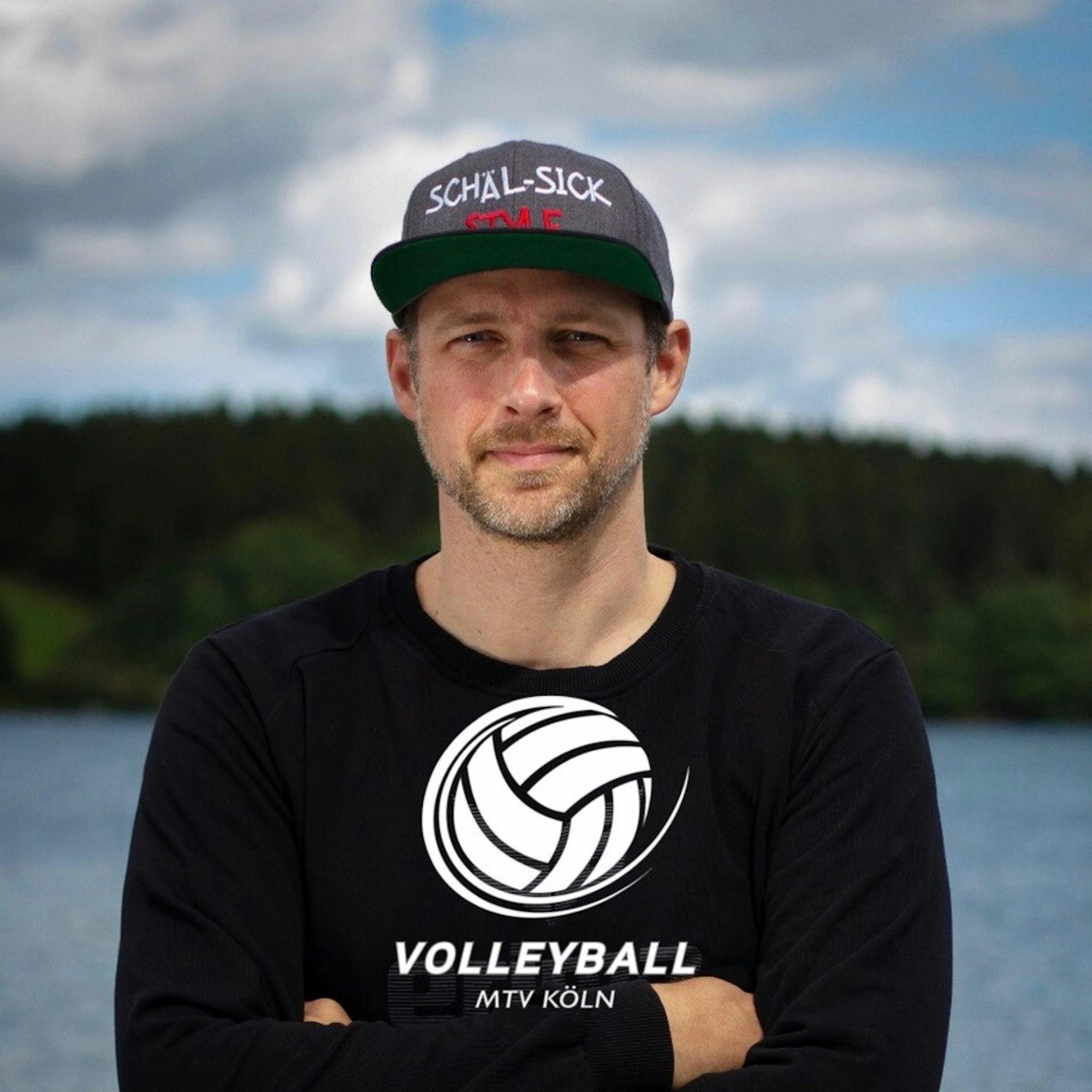 Der Kölner Kai Vogel steht mit einem Volleyball-Pullover vor dem Rhein.