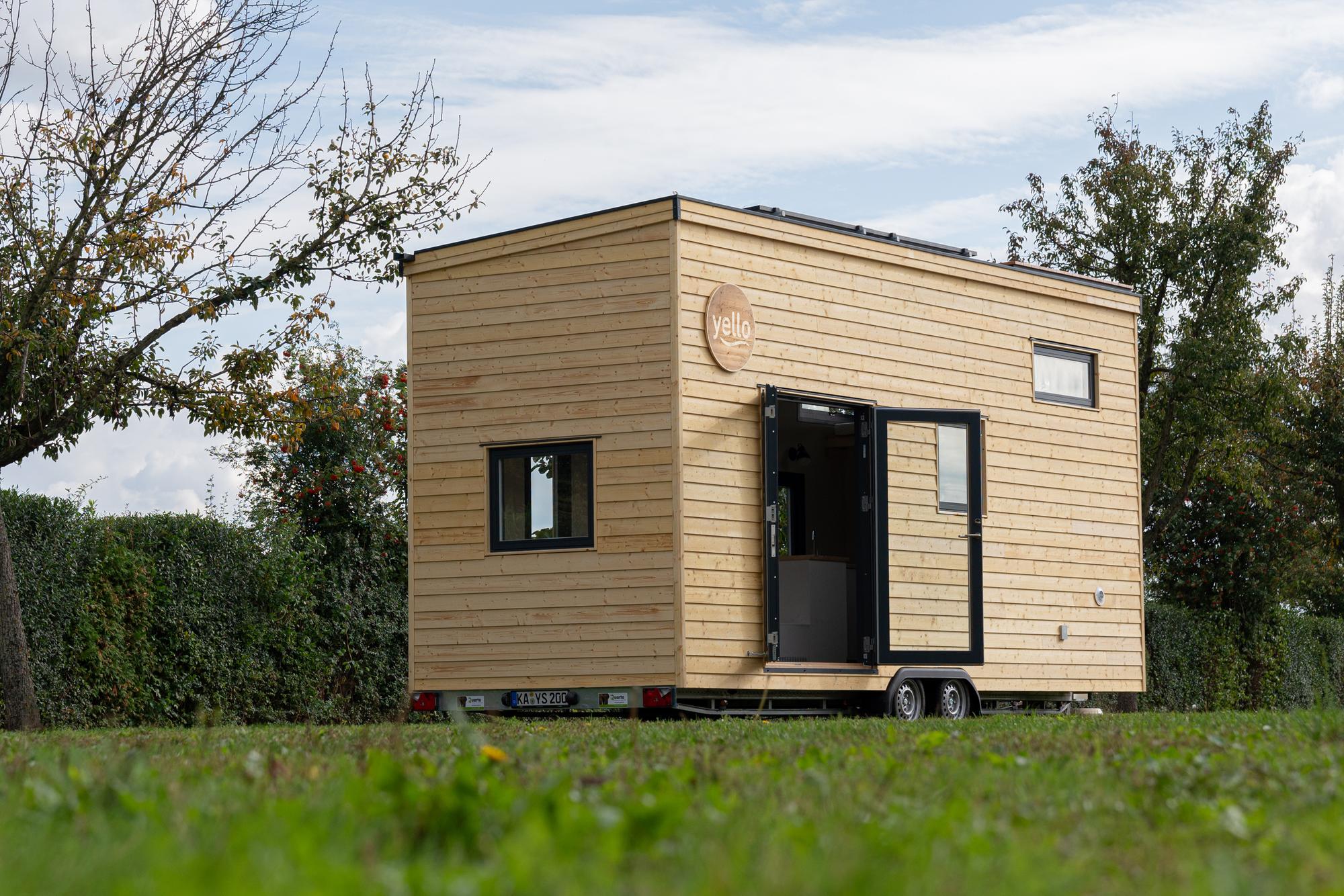 Das Yello Tiny House steht auf einer Wiese.