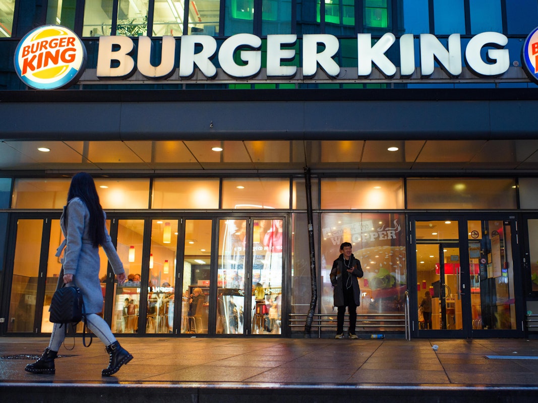 Passanten und Passantinnen gehen am Abend an einer Burger King-Filiale auf dem Alexanderplatz in Berlin vorbei.