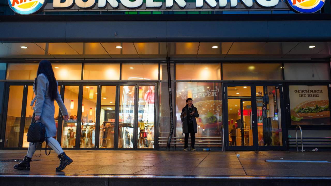 Passanten und Passantinnen gehen am Abend an einer Burger King-Filiale auf dem Alexanderplatz in Berlin vorbei.