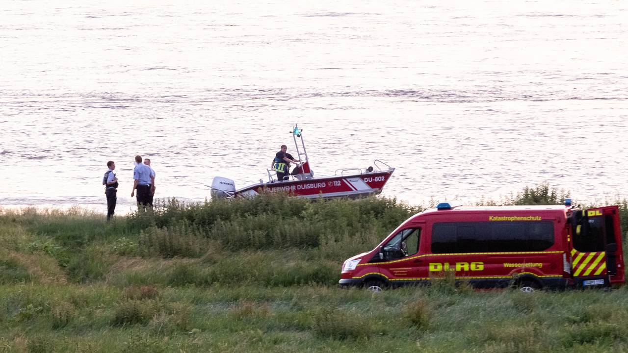 Einsatzkräfte der Polizei, Feuerwehr und DLRG arbeiten am Ufer des Rheins. Auch ein Rettungsboot ist im Einsatz.