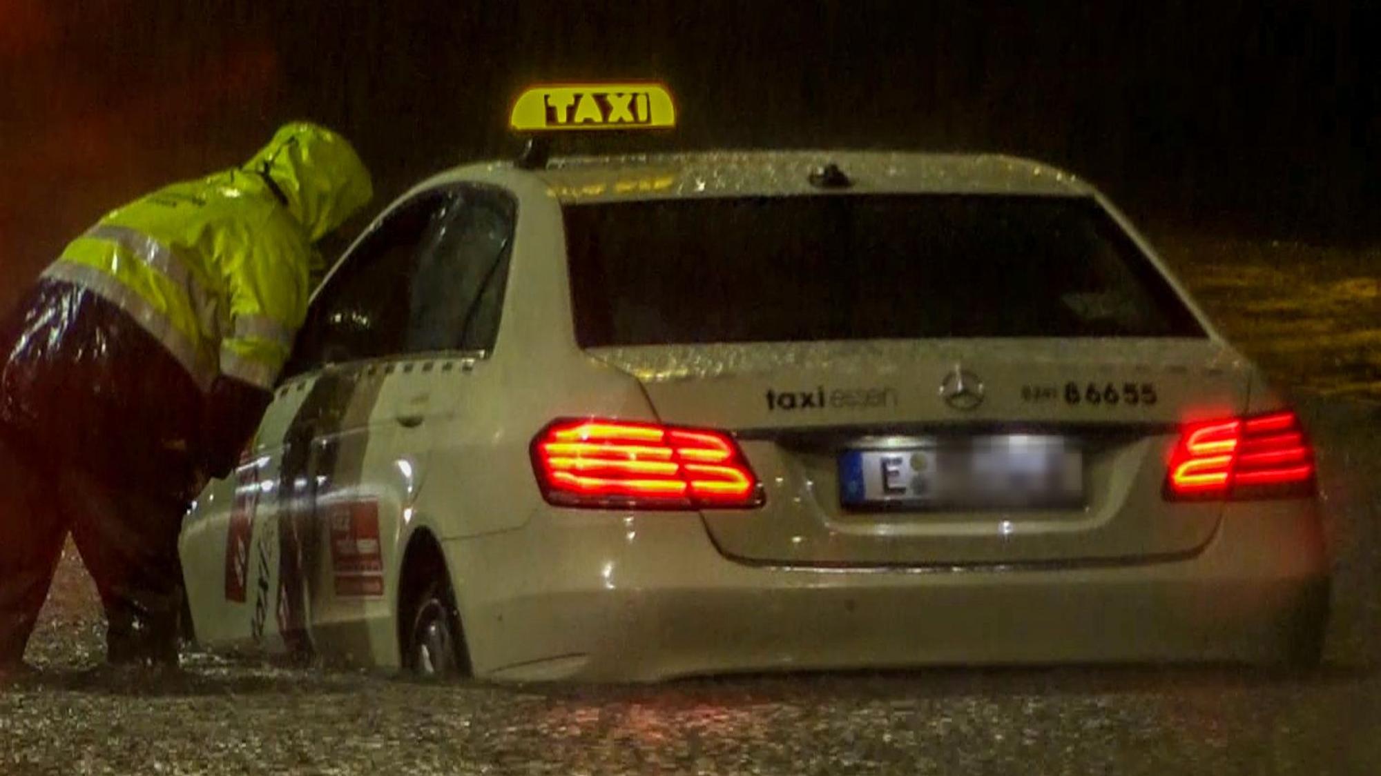 Ein Feuerwehrmann spricht mit dem Fahrer eines Taxis, das sich im Hochwasser festgefahren hat. Starkregen lässt Straßen überfluten.