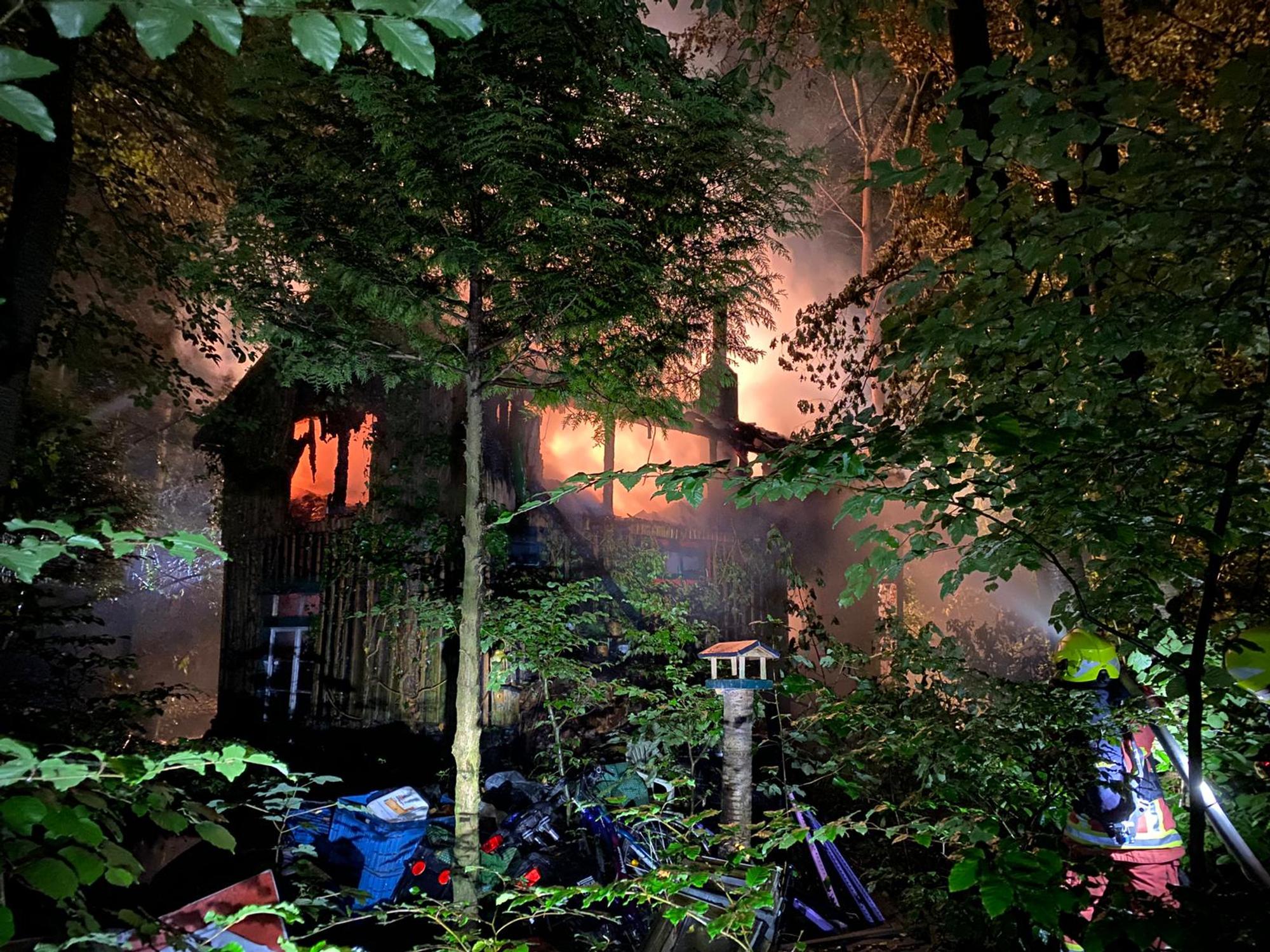 Ein Wohnhaus im Wald steht in Flammen. Feuerwehrleute versuchen, den Brand zu löschen.
