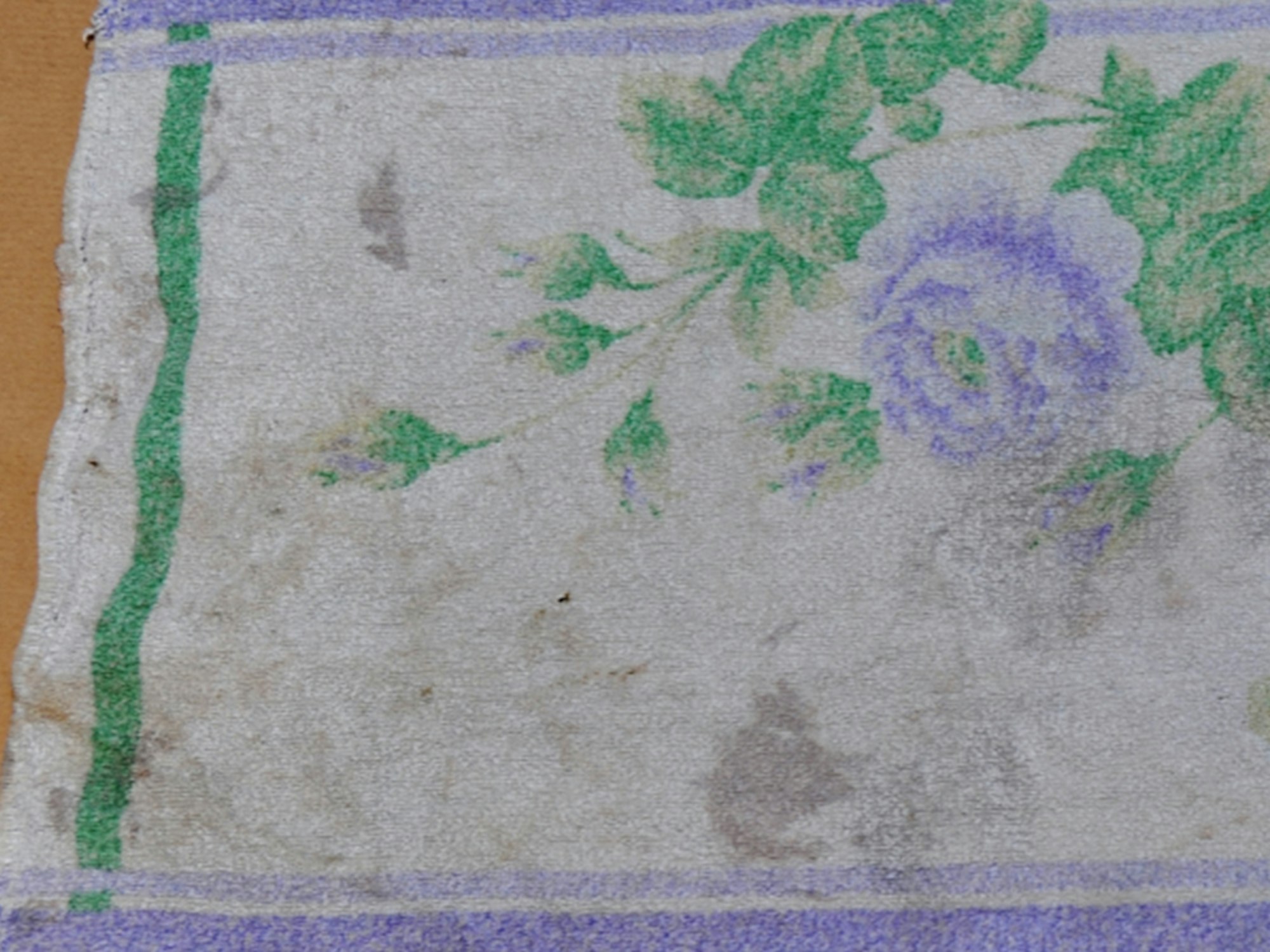 Das verschmutzte Handtuch hat ein Blumenmuster mit grüner sowie lilafarbener Umrandung.