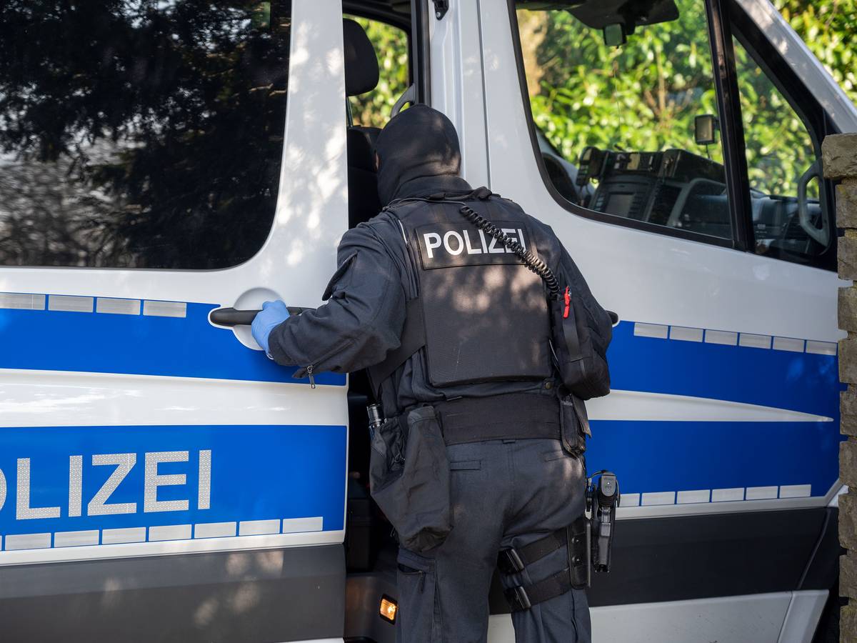 Ein Polizist steht im Rahmen einer Razzia an einem Polizeifahrzeug und sieht hinein.