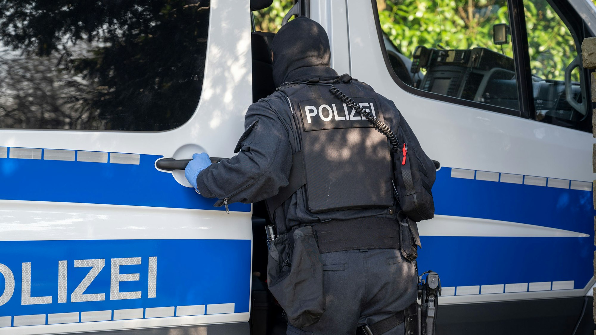 Ein Polizist steht im Rahmen einer Razzia an einem Polizeifahrzeug und sieht hinein.