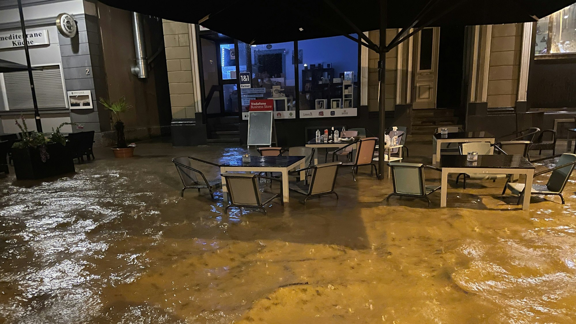 Tische und Stühle sind in Hagen halb von Wasser überflutet, sie stehen vor einem Hauseingang.
