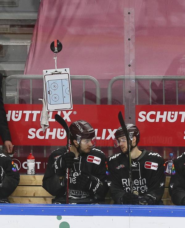 Uwe Krupp beobachtet ein DEL-Spiel der Kölner Haie am Spielfeldrand hinter seinen Ersatzspielern.