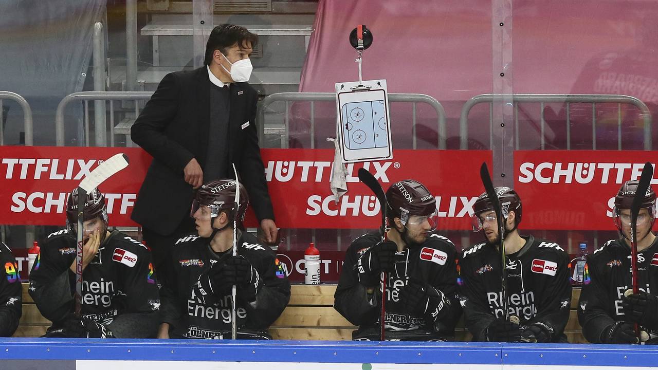 Uwe Krupp beobachtet ein DEL-Spiel der Kölner Haie am Spielfeldrand hinter seinen Ersatzspielern.