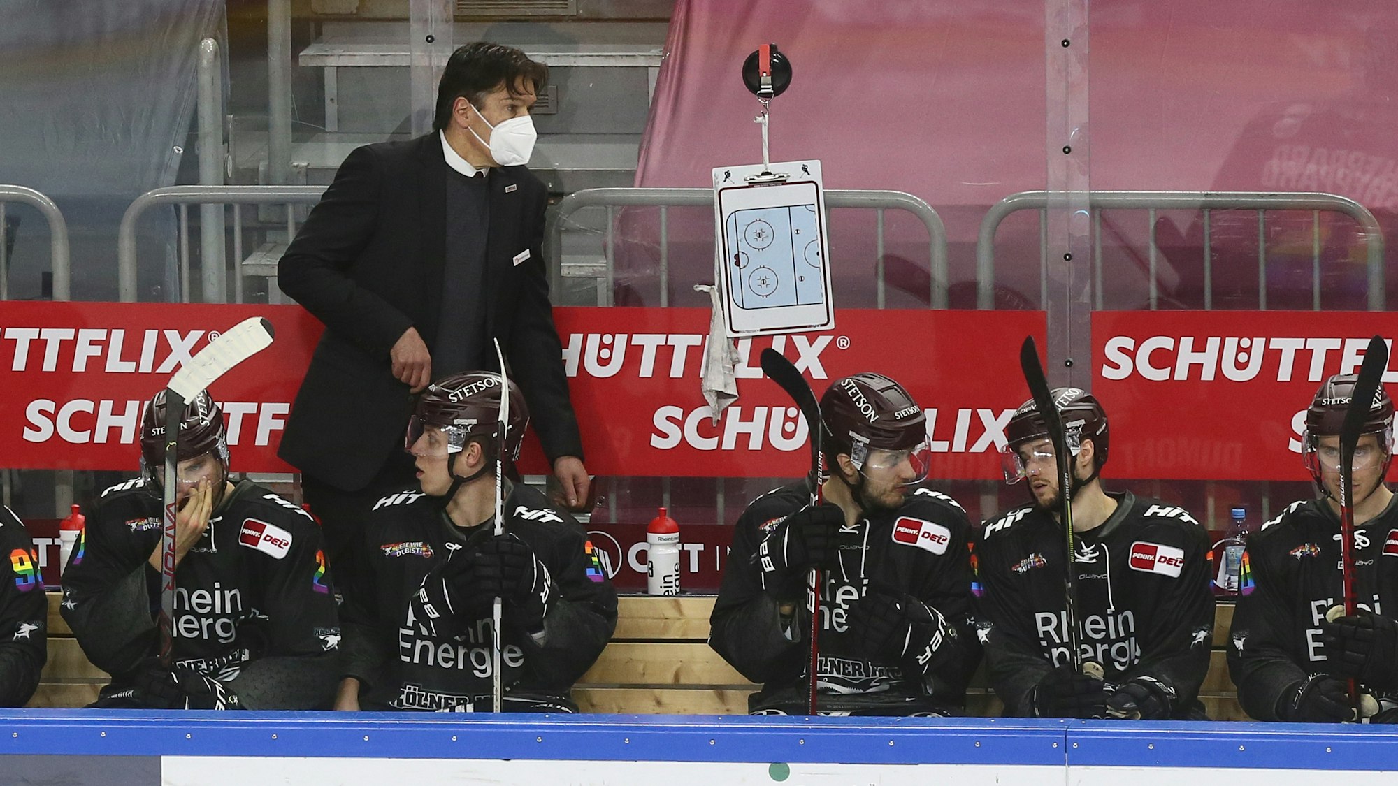 Uwe Krupp beobachtet ein DEL-Spiel der Kölner Haie am Spielfeldrand hinter seinen Ersatzspielern.