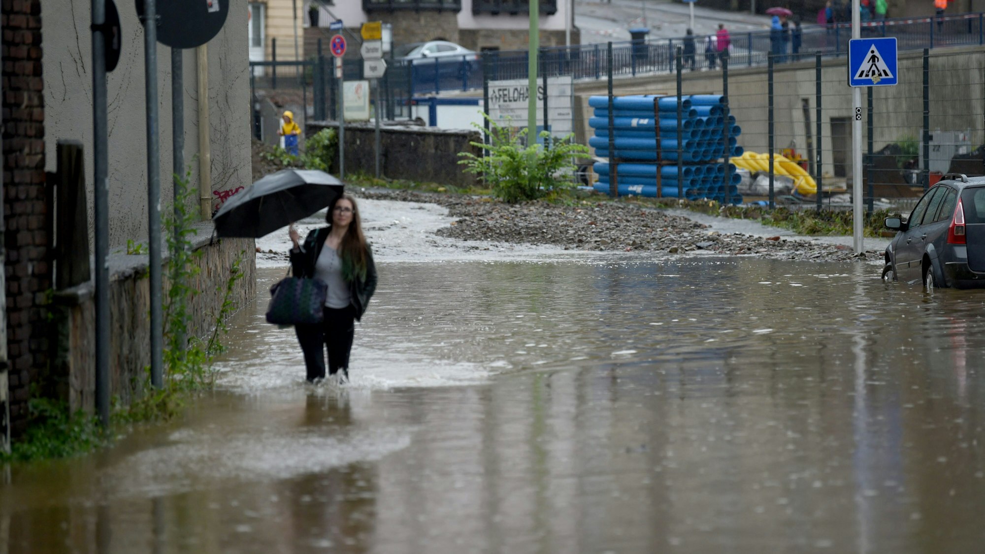 Unwetter in NRW. Eine Frau läuft mit Regenschirm durch eine überflutete Straße in Hagen.