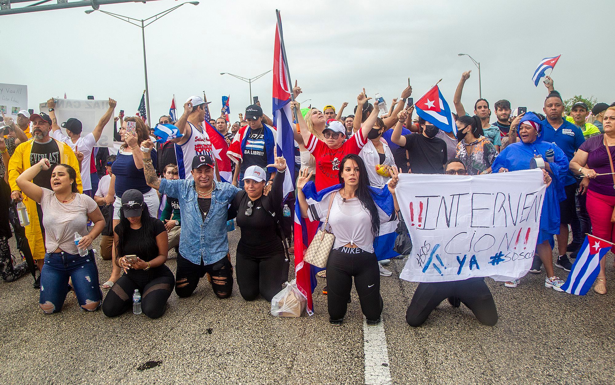Mehrere Menschen versammeln sich in Miami (USA) mit Fahnen von Kuba und Postern auf dem Palmetto Expressway am Coral Way zur Unterstützung der Demonstranten in Kuba. Sie sind symbolisch auf die Knie gegangen.
