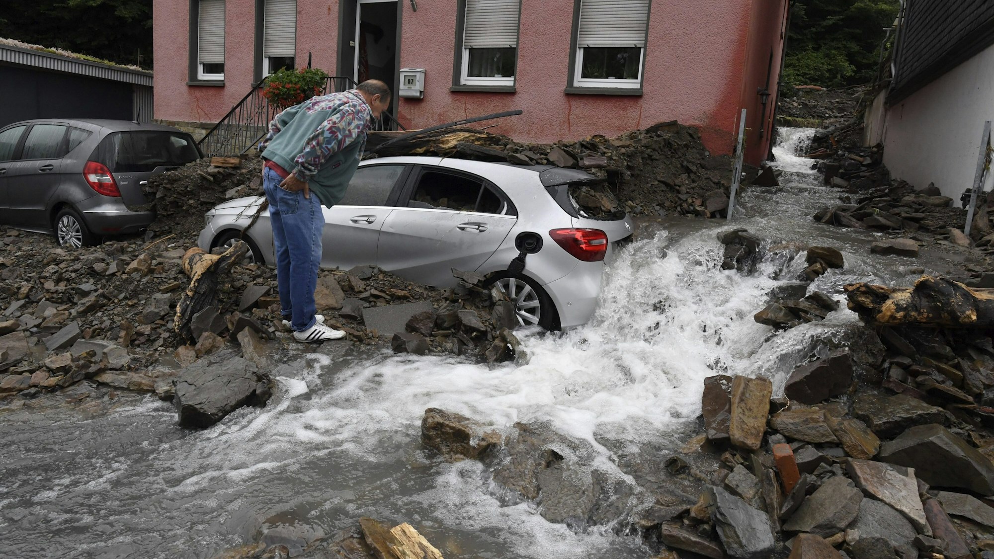 Ein Anwohner schaut sich am Donnerstag (15. Juli) die Schäden in Hagen an, die die Überflutung der Nahma am Vorabend mit sich gebracht hat. Durch die heftigen Regenfälle war das Flüsschen zum reissenden Fluss geworden, ein silbernes Auto steht inmitten des Stroms und dem vielen Geröll, das er mit sich gerissen hat.