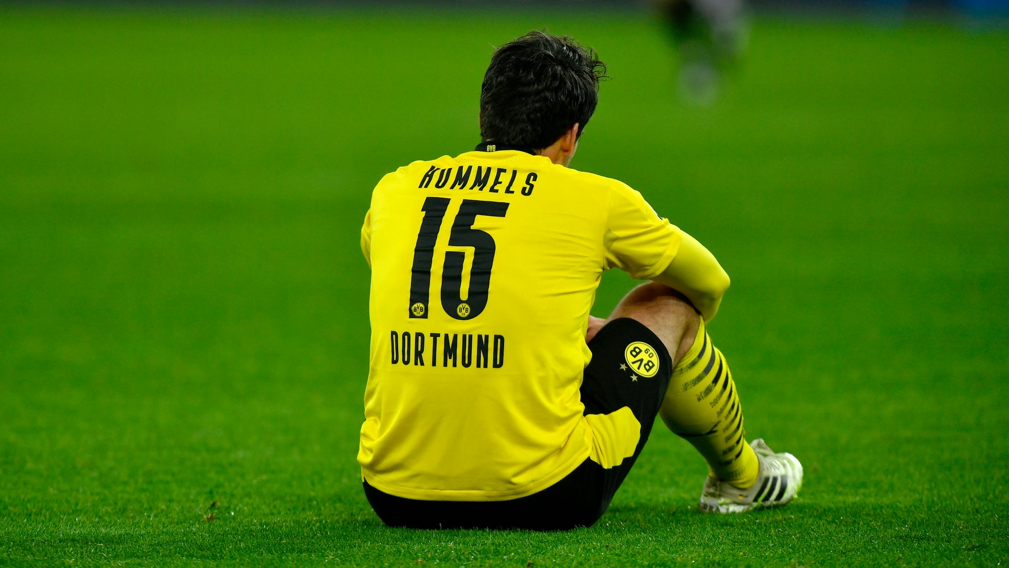 Mats Hummels sitzt auf dem Rasen mit den Armen auf den Knien gestützt