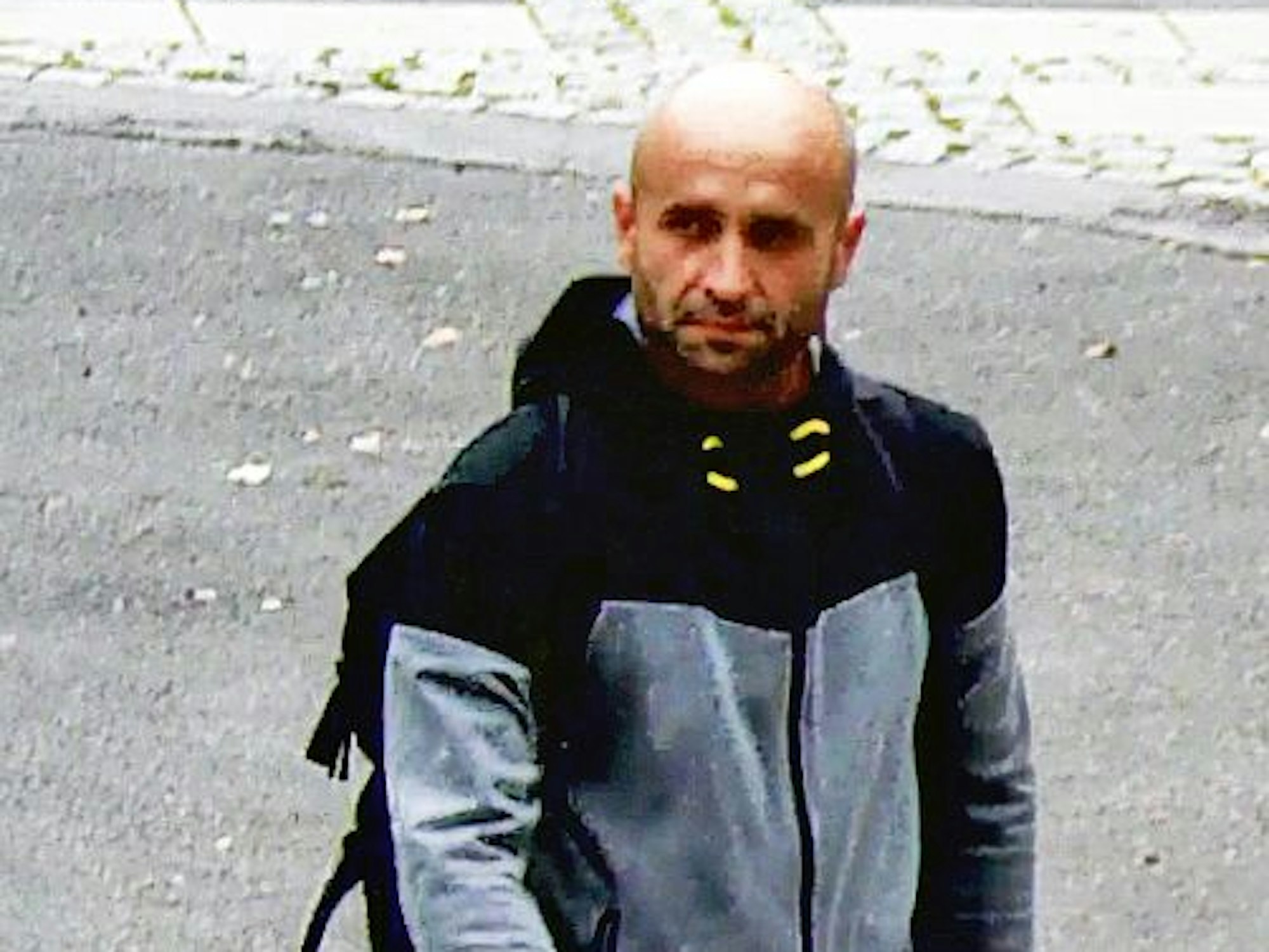 Ein Mann mit Glatze geht über einen asphaltierten Platz.