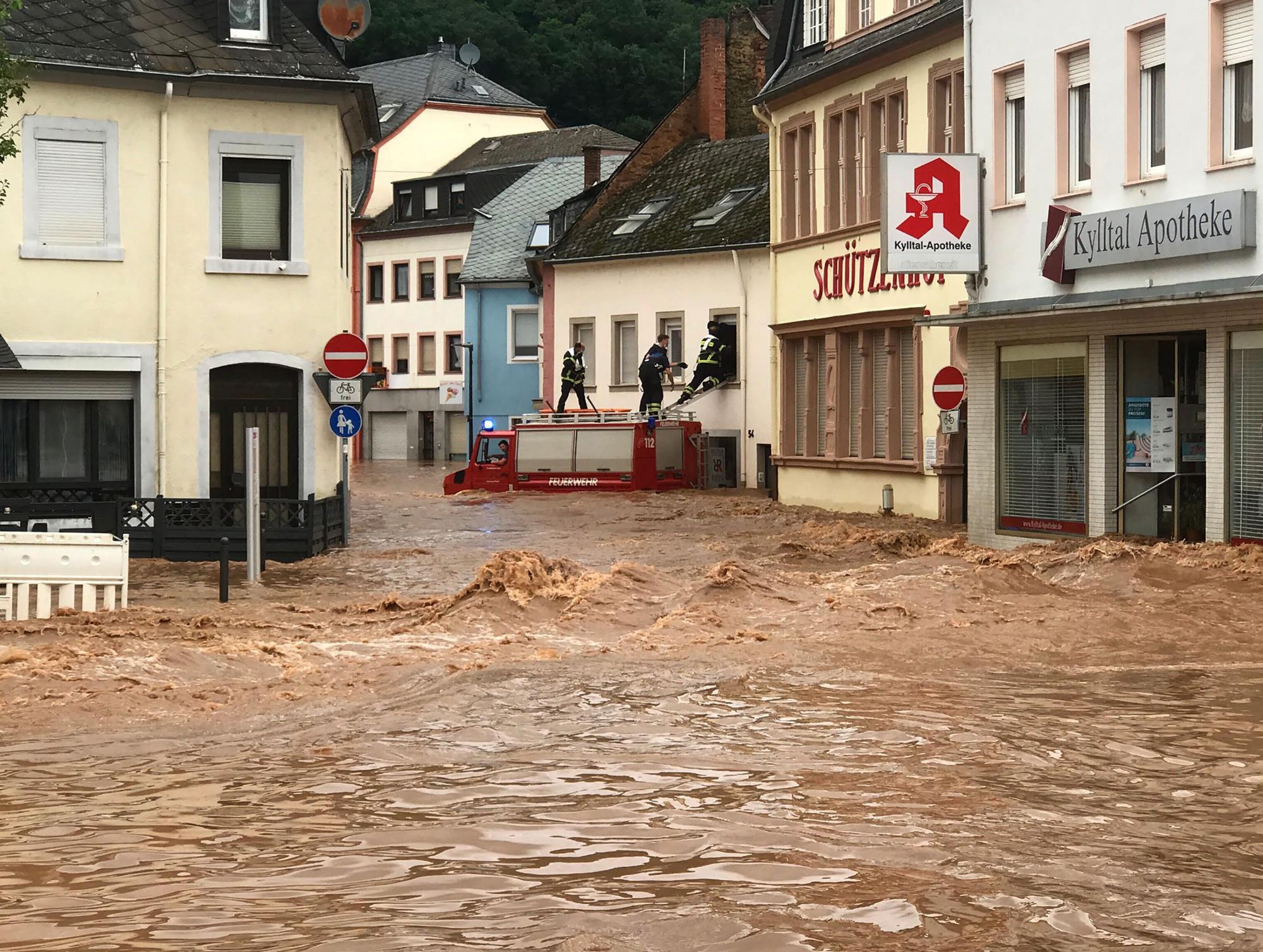 Feuerwehrmänner stehen auf einem Einsatzwagen, der in den Fluten steht.