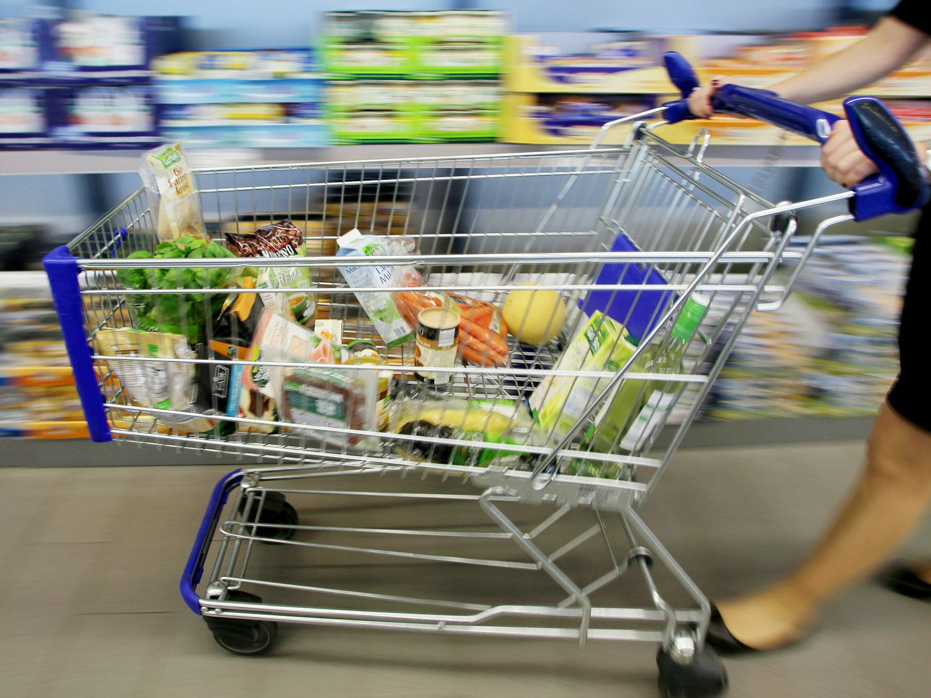 Kundin fährt gefüllten Einkaufswagen durch Aldi-Filiale.