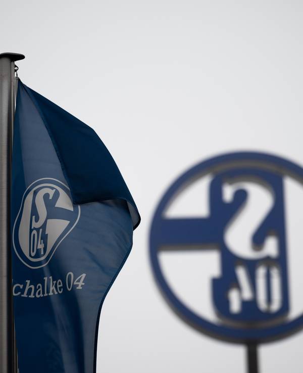 Eine Fahne mit dem Logo des FC Schalke 04 weht vor grauem Himmel.