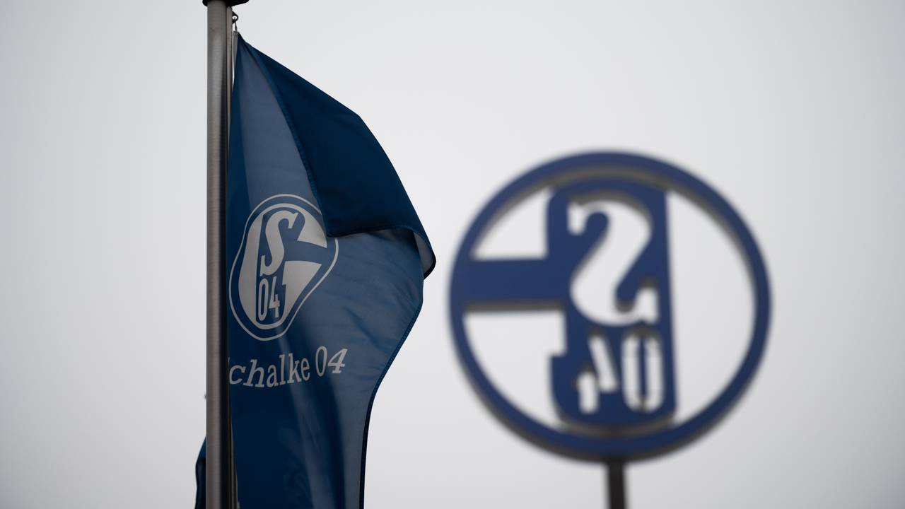 Eine Fahne mit dem Logo des FC Schalke 04 weht vor grauem Himmel.