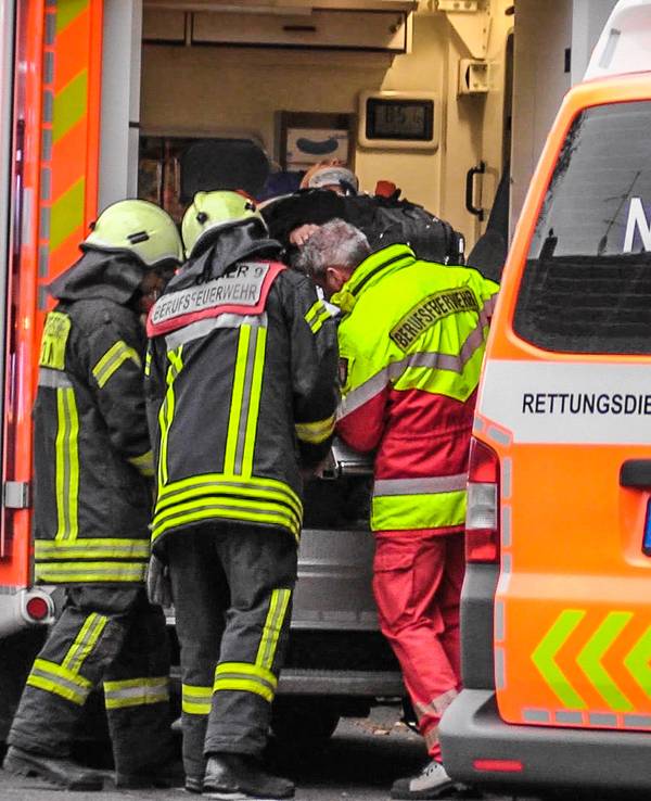 Drei Feuerwehrmänner schieben einen Verletzten in einen Rettungswagen.