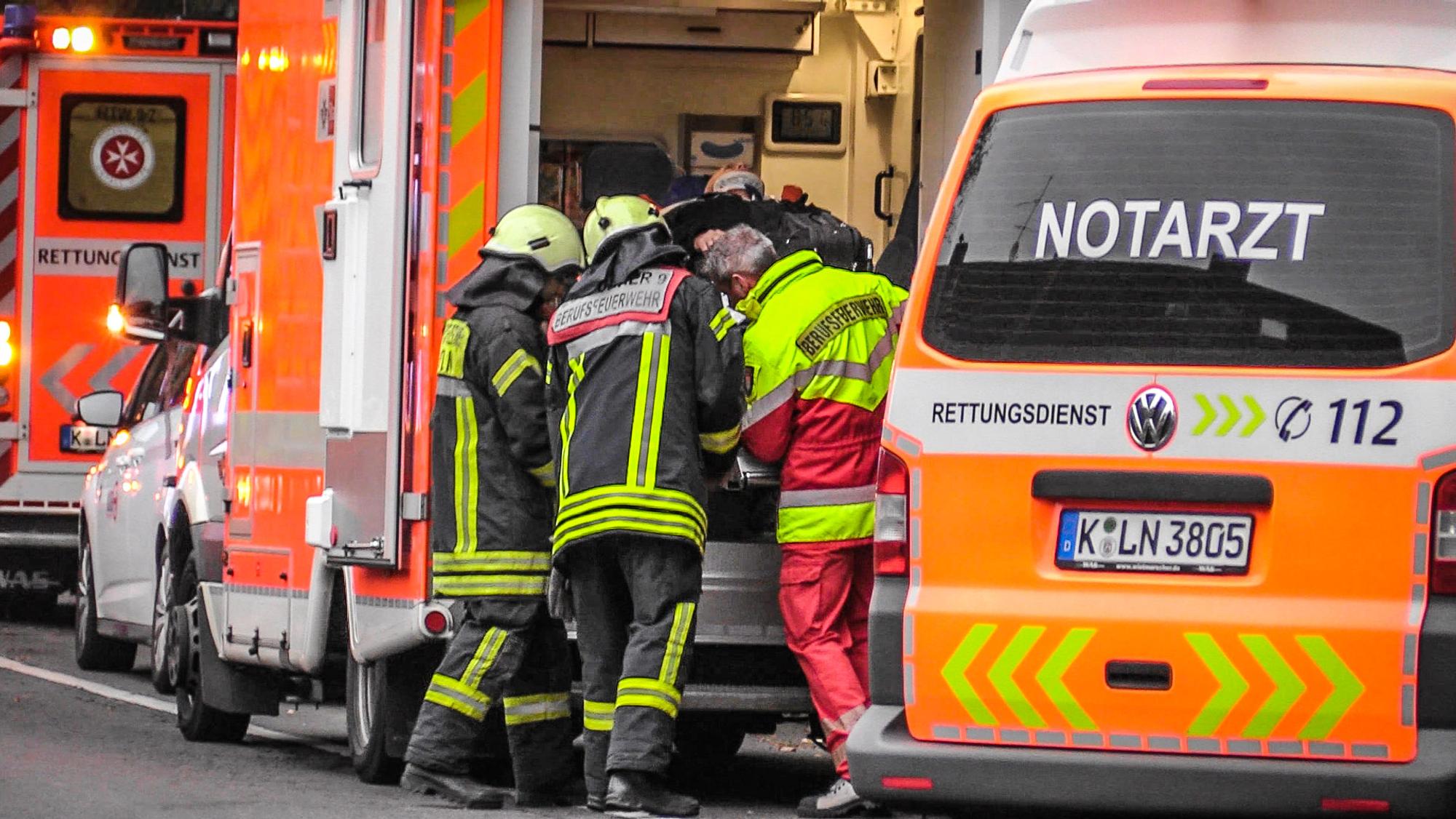 Drei Feuerwehrmänner schieben einen Verletzten in einen Rettungswagen.