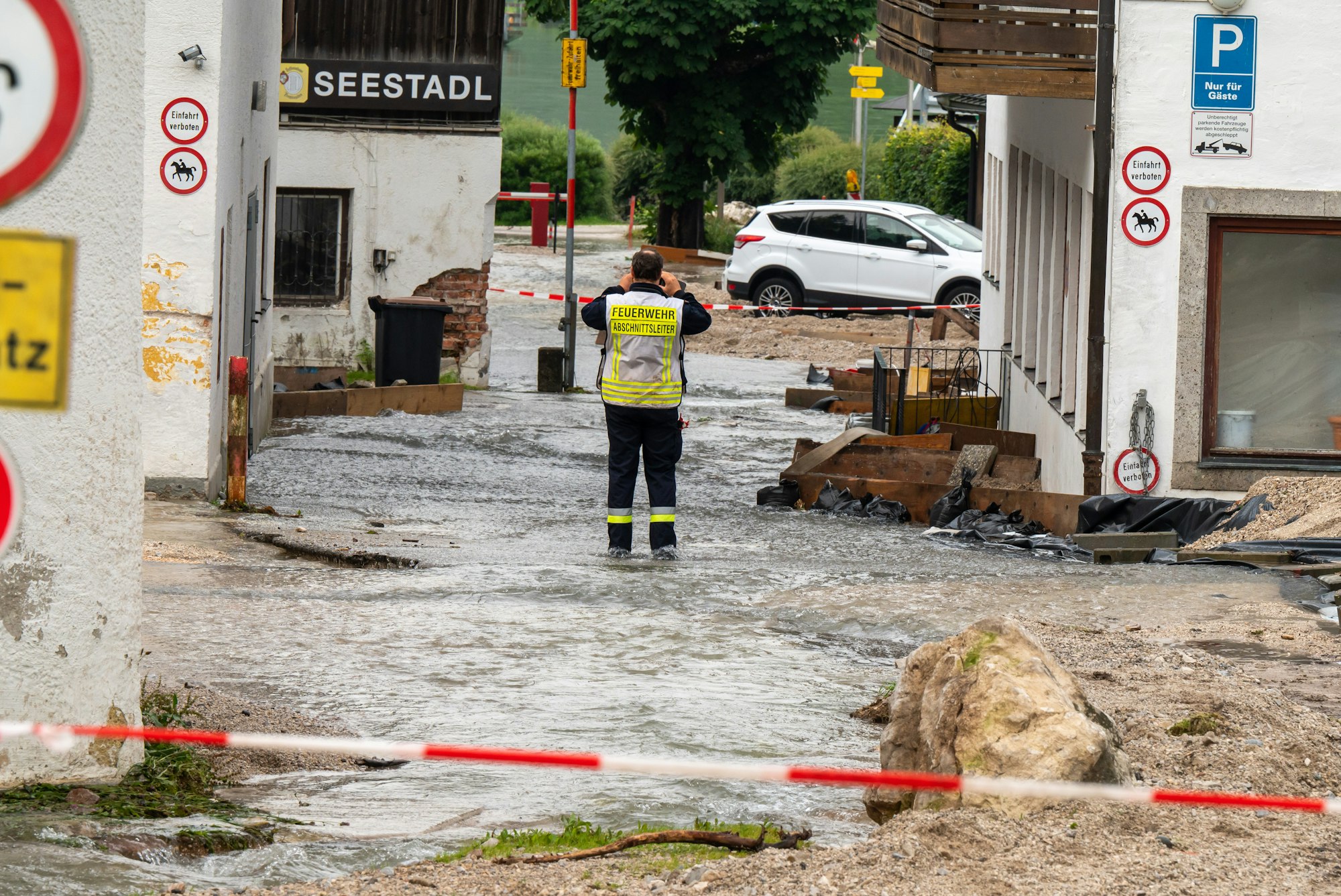 Ein Feuerwehrmann steht auf einer Straße, die zum Königssee führt, und über die noch Wasser abfließt.