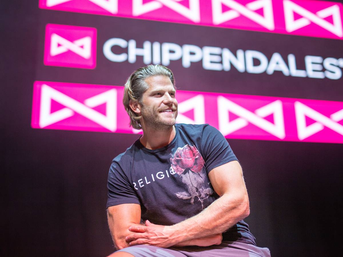 Paul Janke gibt es jetzt auf Onlyfans. Hier sitzt er in München vor dem Logo der Strippercombo Chippendales.