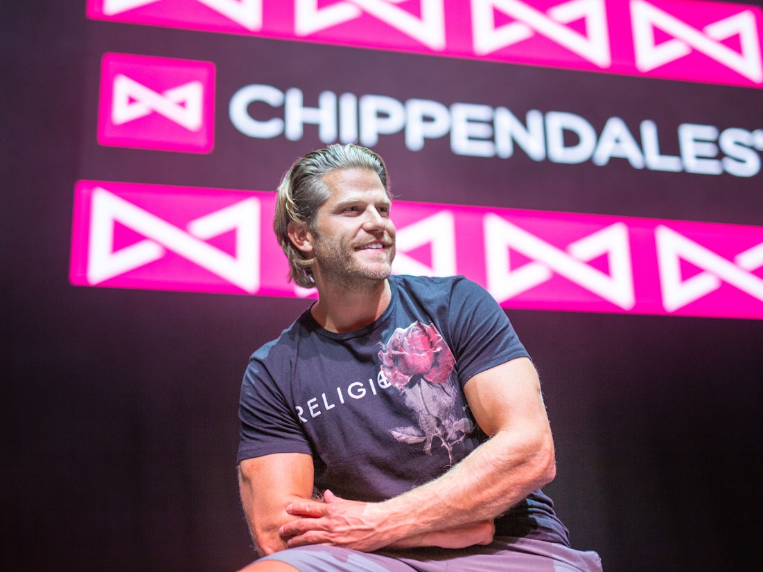 Paul Janke gibt es jetzt auf Onlyfans. Hier sitzt er in München vor dem Logo der Strippercombo Chippendales.