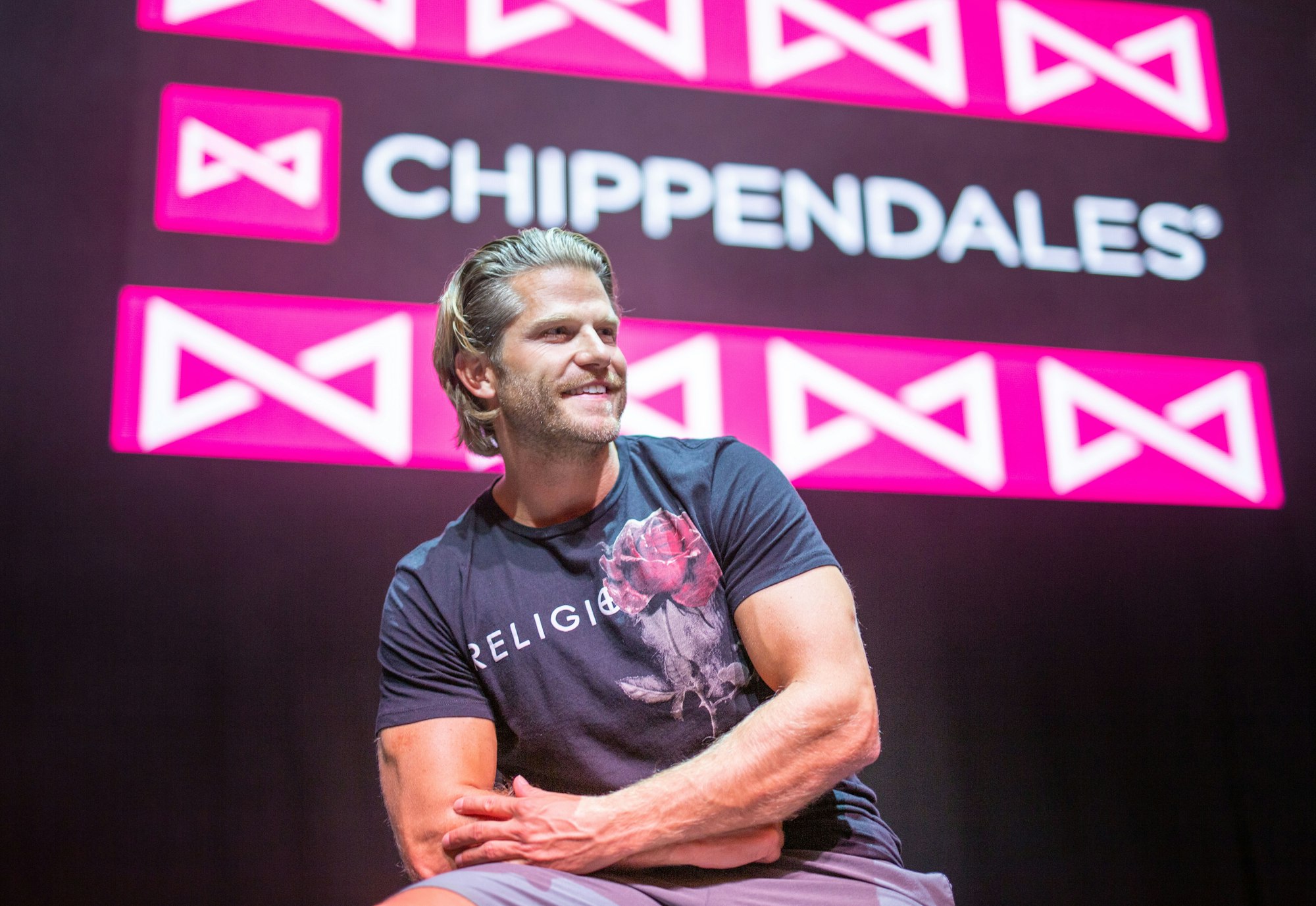 Paul Janke gibt es jetzt auf Onlyfans. Hier sitzt er in München vor dem Logo der Strippercombo Chippendales.