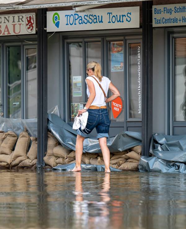 Eine Frau geht in Passau an der Uferpromenade an einem Reise-Center vorbei, das mit Sandsäcke vor den Türen vor dem Wasser der Donau abgedichtet wurde.