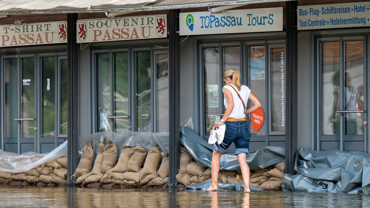 Eine Frau geht in Passau an der Uferpromenade an einem Reise-Center vorbei, das mit Sandsäcke vor den Türen vor dem Wasser der Donau abgedichtet wurde.