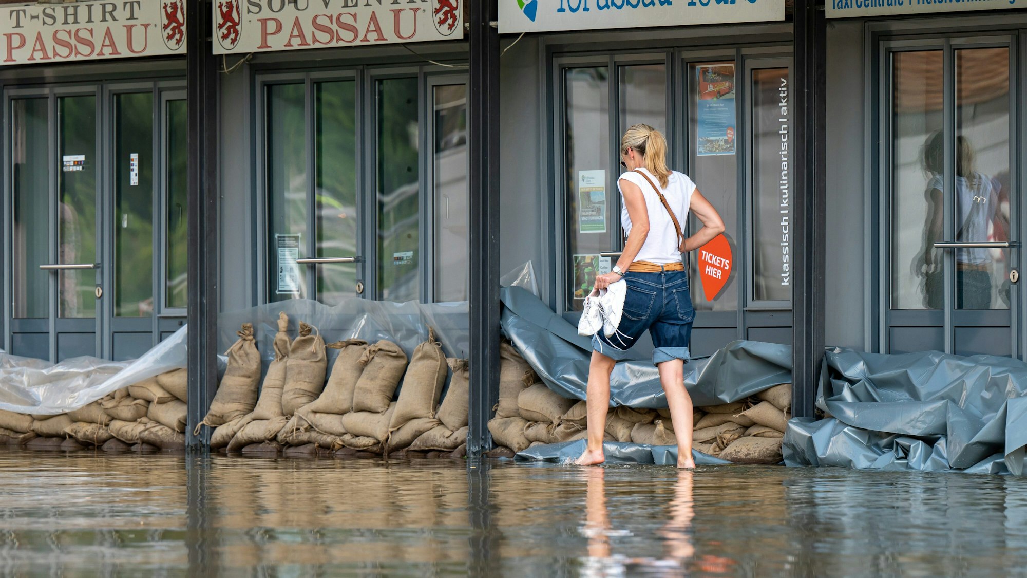 Eine Frau geht in Passau an der Uferpromenade an einem Reise-Center vorbei, das mit Sandsäcke vor den Türen vor dem Wasser der Donau abgedichtet wurde.