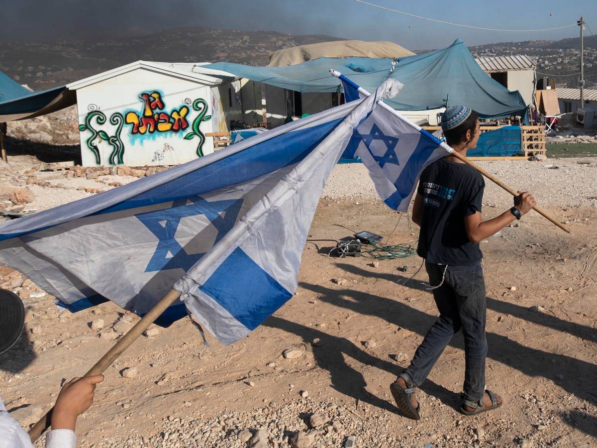 Zwei Menschen schwenken in einer Siedlung Israel-Flaggen im Westjordanland.