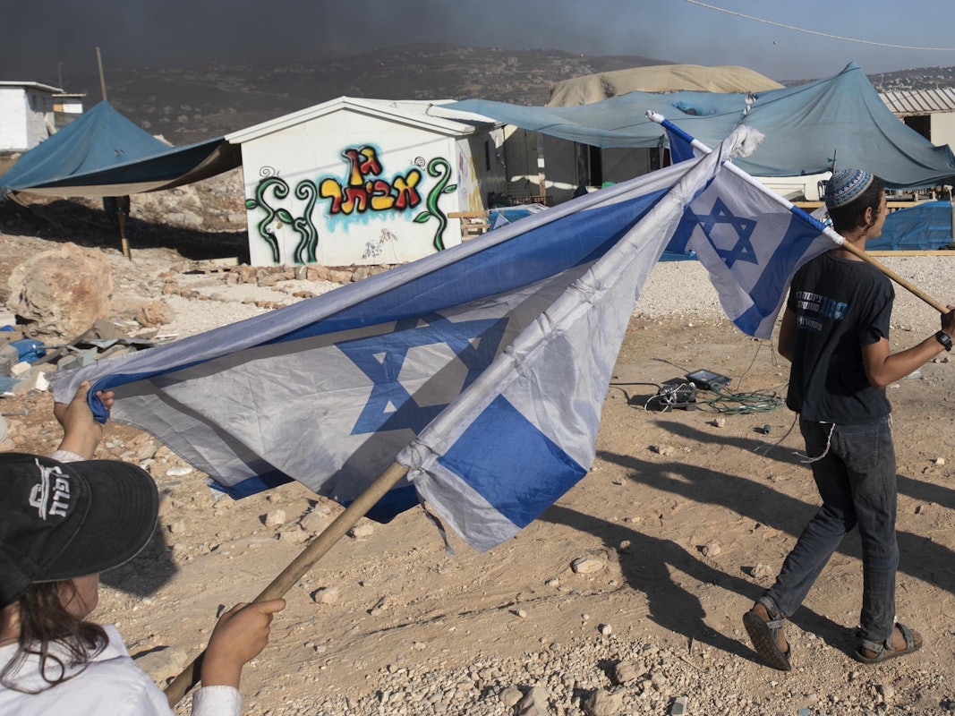 Zwei Menschen schwenken in einer Siedlung Israel-Flaggen im Westjordanland.