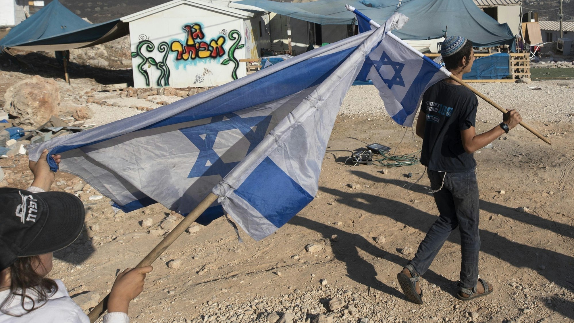 Zwei Menschen schwenken in einer Siedlung Israel-Flaggen im Westjordanland.