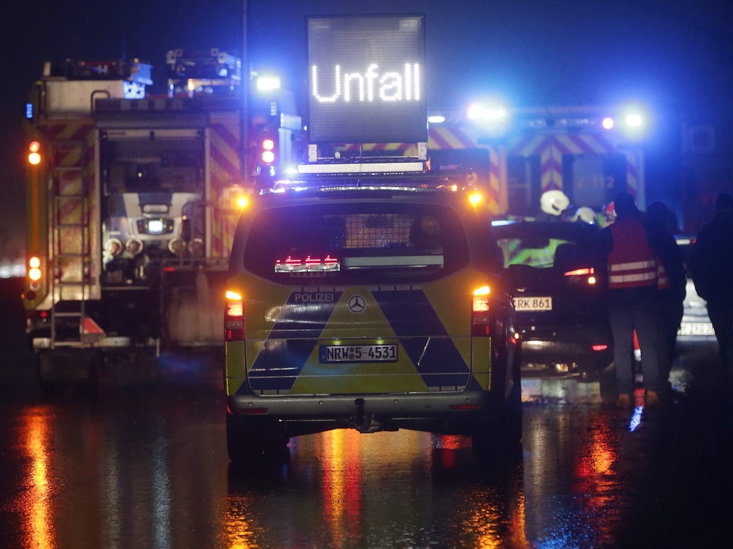 Polizei- und Feuerwehrfahrzeuge mit Blaulicht sichern eine Unfallstelle auf der Autobahn.