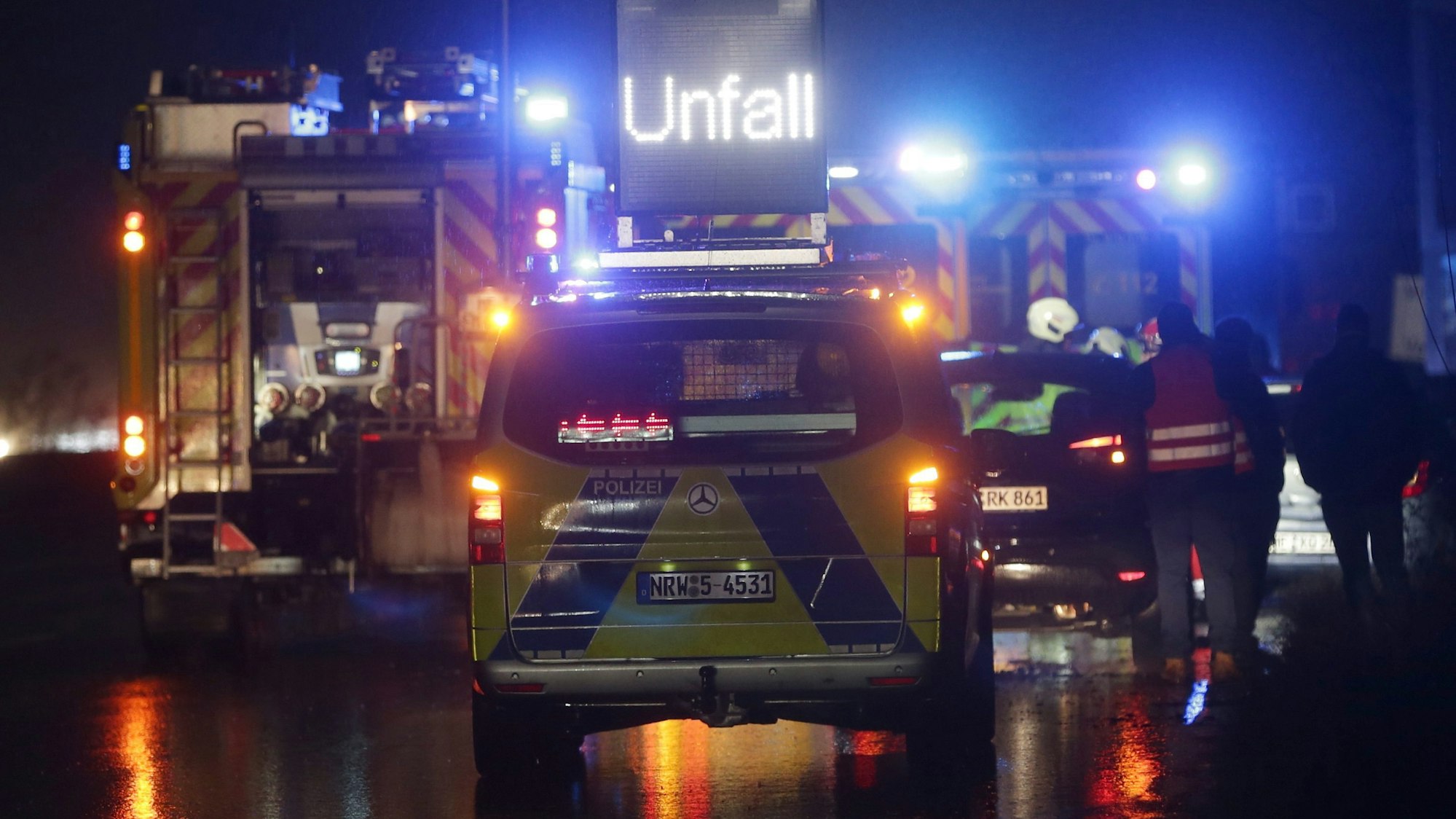 Polizei- und Feuerwehrfahrzeuge mit Blaulicht sichern eine Unfallstelle auf der Autobahn.