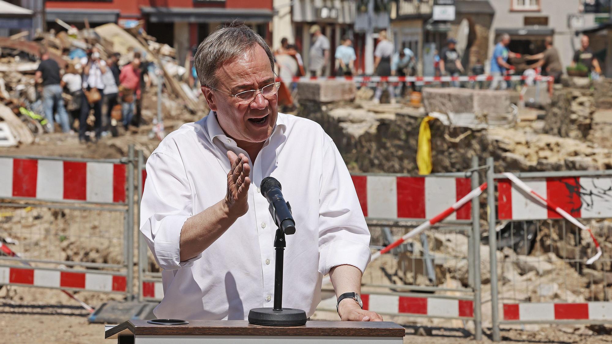 Armin Laschet spricht in ein Mikrofon. Im Hintergrund sieht man die Unwetterschäden in Bad Münstereifel, die mit einem Bauzaun abgesperrt sind.