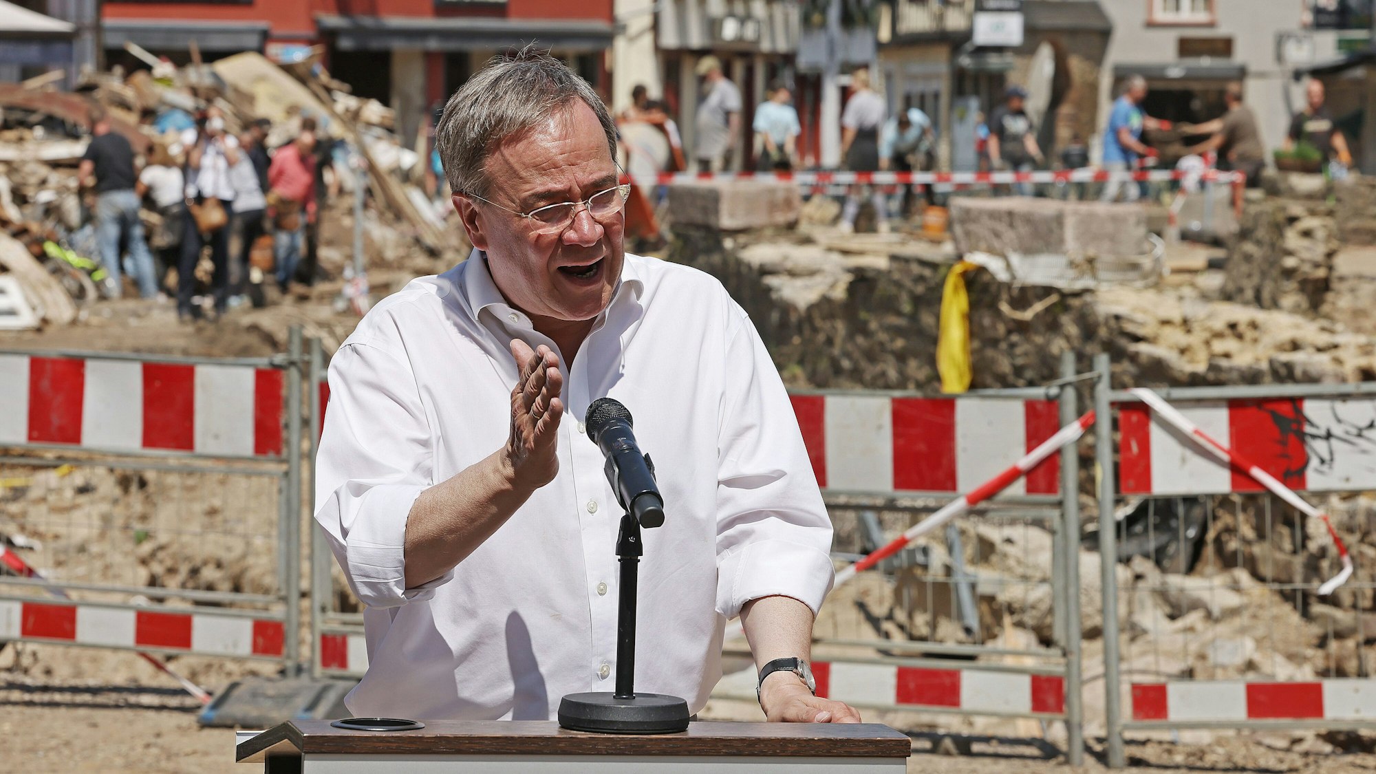 Armin Laschet spricht in ein Mikrofon. Im Hintergrund sieht man die Unwetterschäden in Bad Münstereifel, die mit einem Bauzaun abgesperrt sind.
