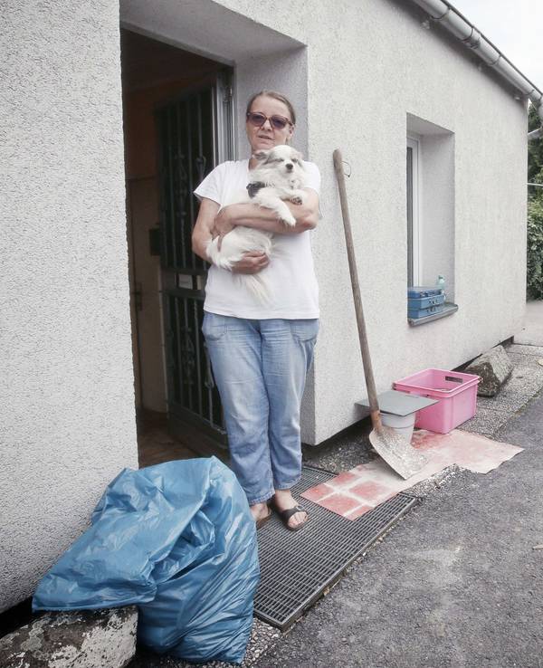 Eine Frau steht mit ihrem Hund vor ihrem Haus, das beim Hochwasser in Düsseldorf beschädigt wurde.