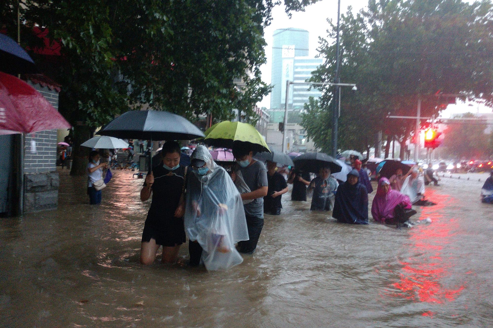 Menschen waten in der zentralchinesischen Provinz Henan durch eine überflutete Straße.