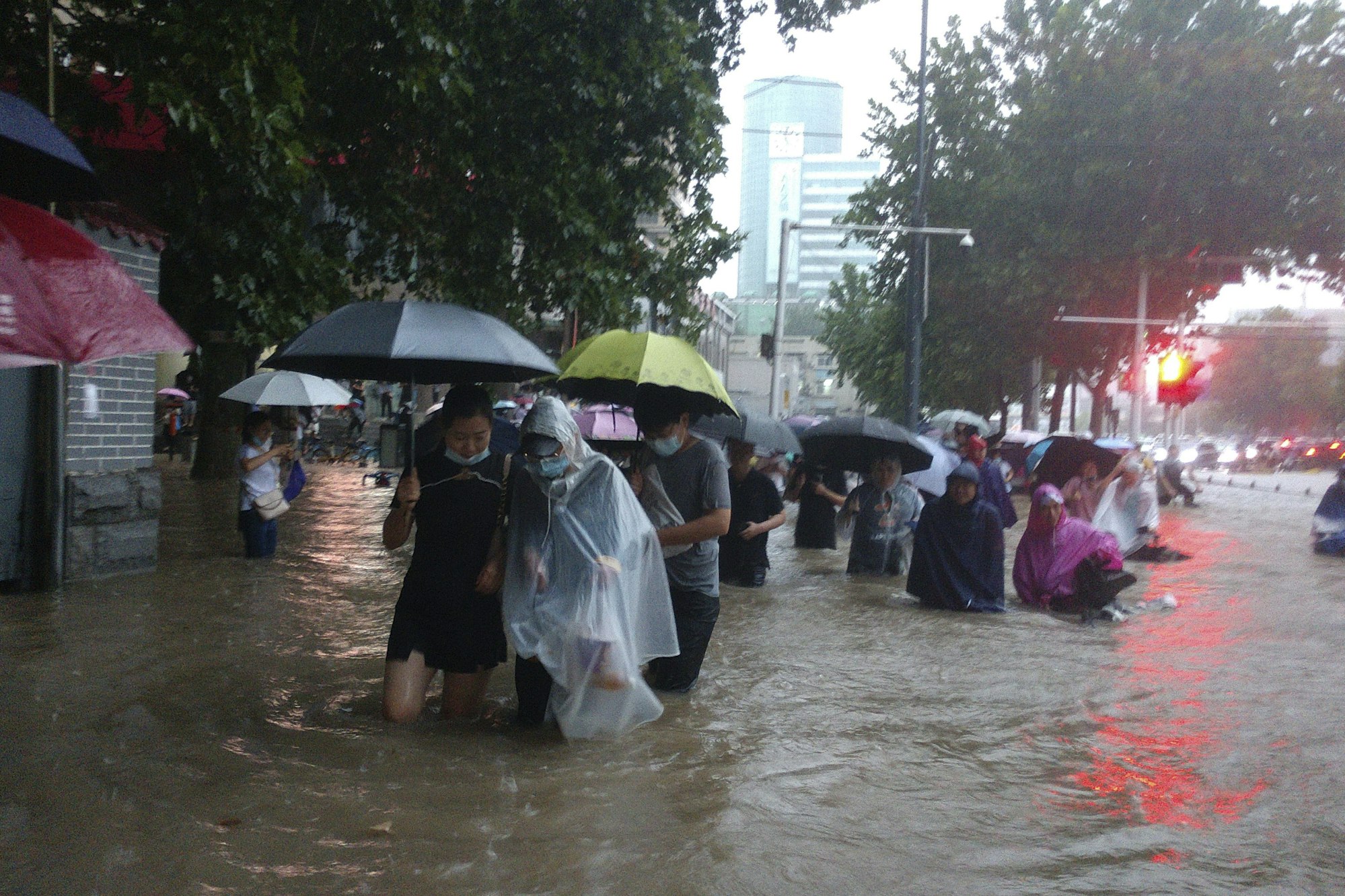 Menschen waten in der zentralchinesischen Provinz Henan durch eine überflutete Straße.