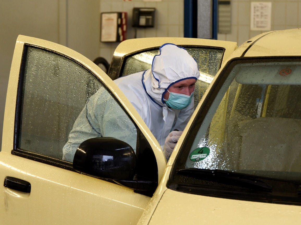 Ein Mann in einem weißen Ganzkörperanzug beugt sich in ein Auto.